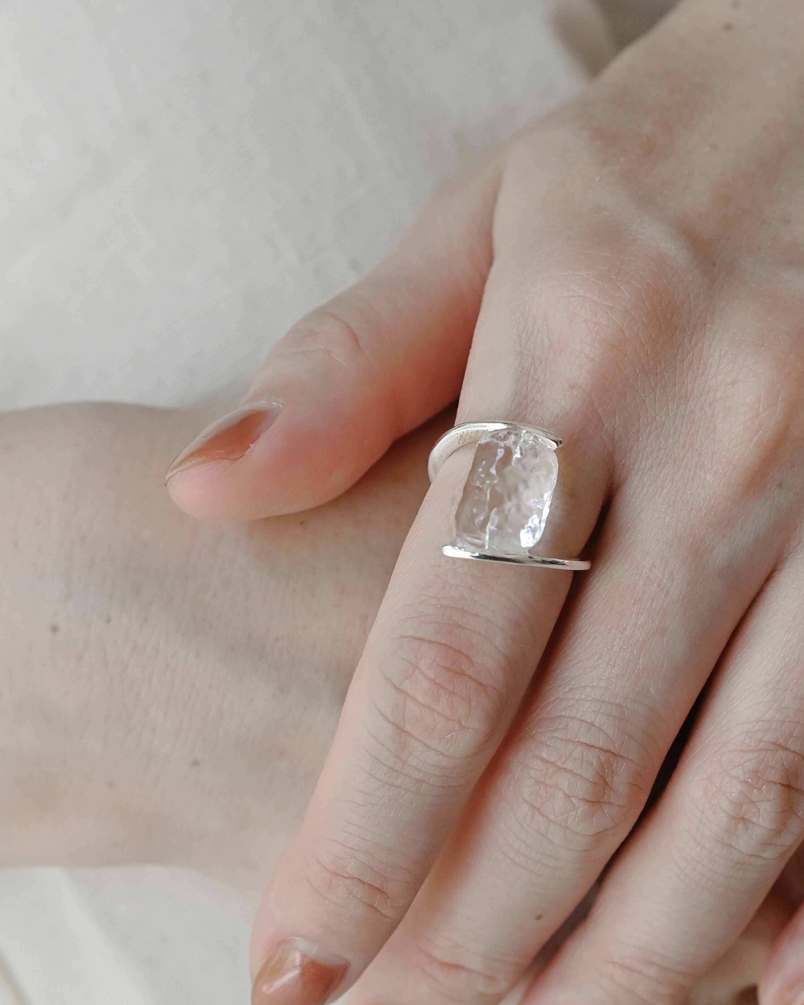 A rhodium‑color plated ring featuring clear glass fragments inspired by melting glaciers, held between two metal bands.