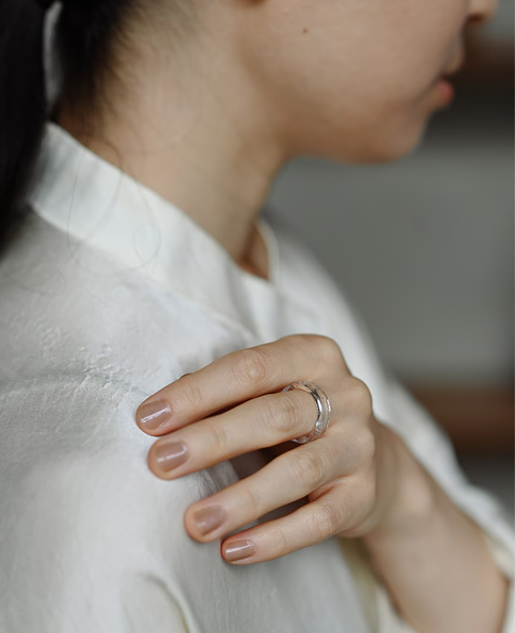 A clear glass ring whose rippled surface evokes the texture of water, shining with a clean, transparent glow.