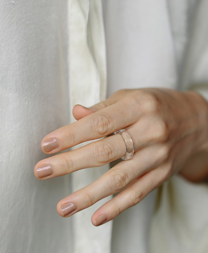 A clear glass ring with soft, rippling textures that reflect light like the surface of water.