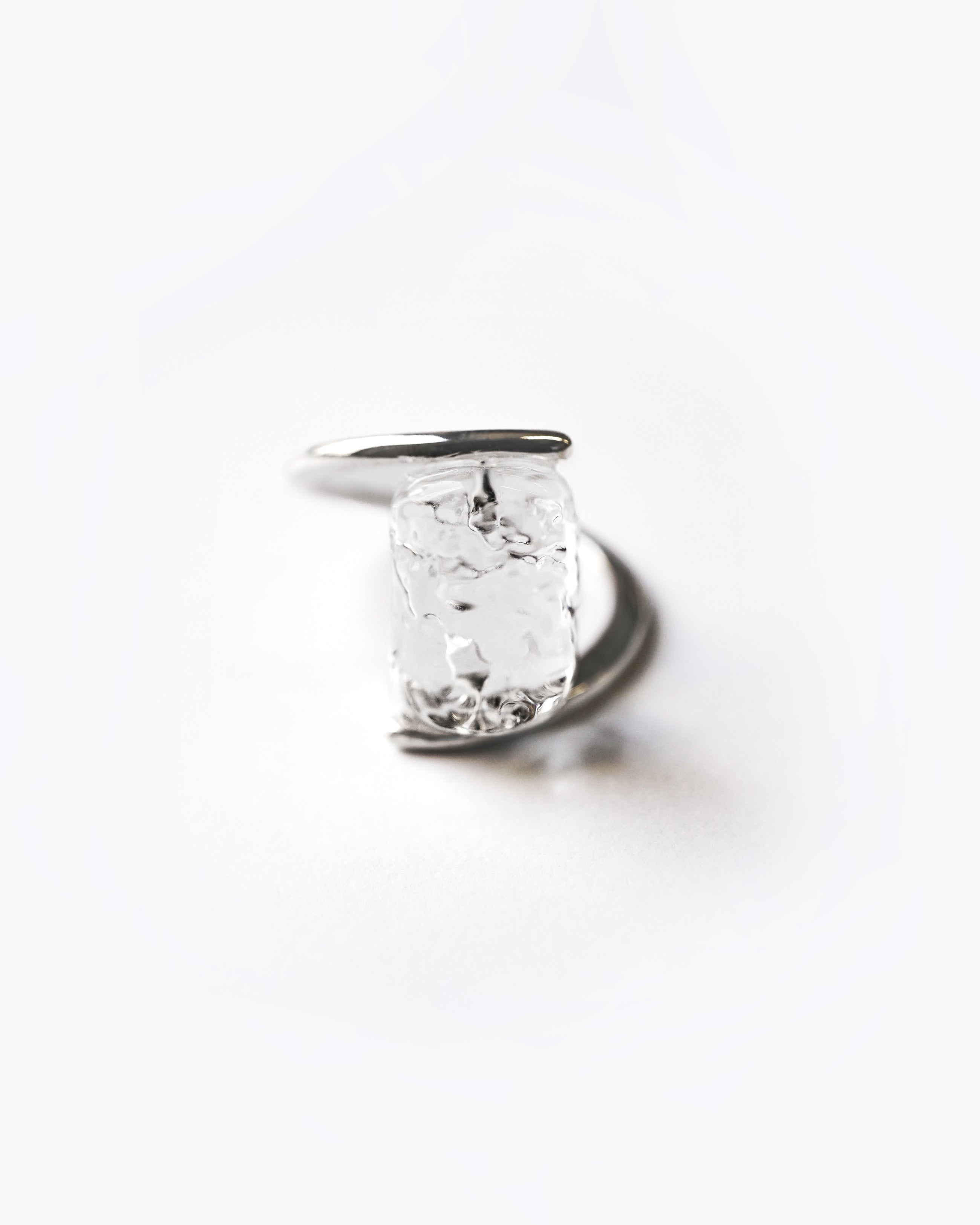 A rhodium‑color plated ring featuring clear glass fragments inspired by melting glaciers, held between two metal bands.