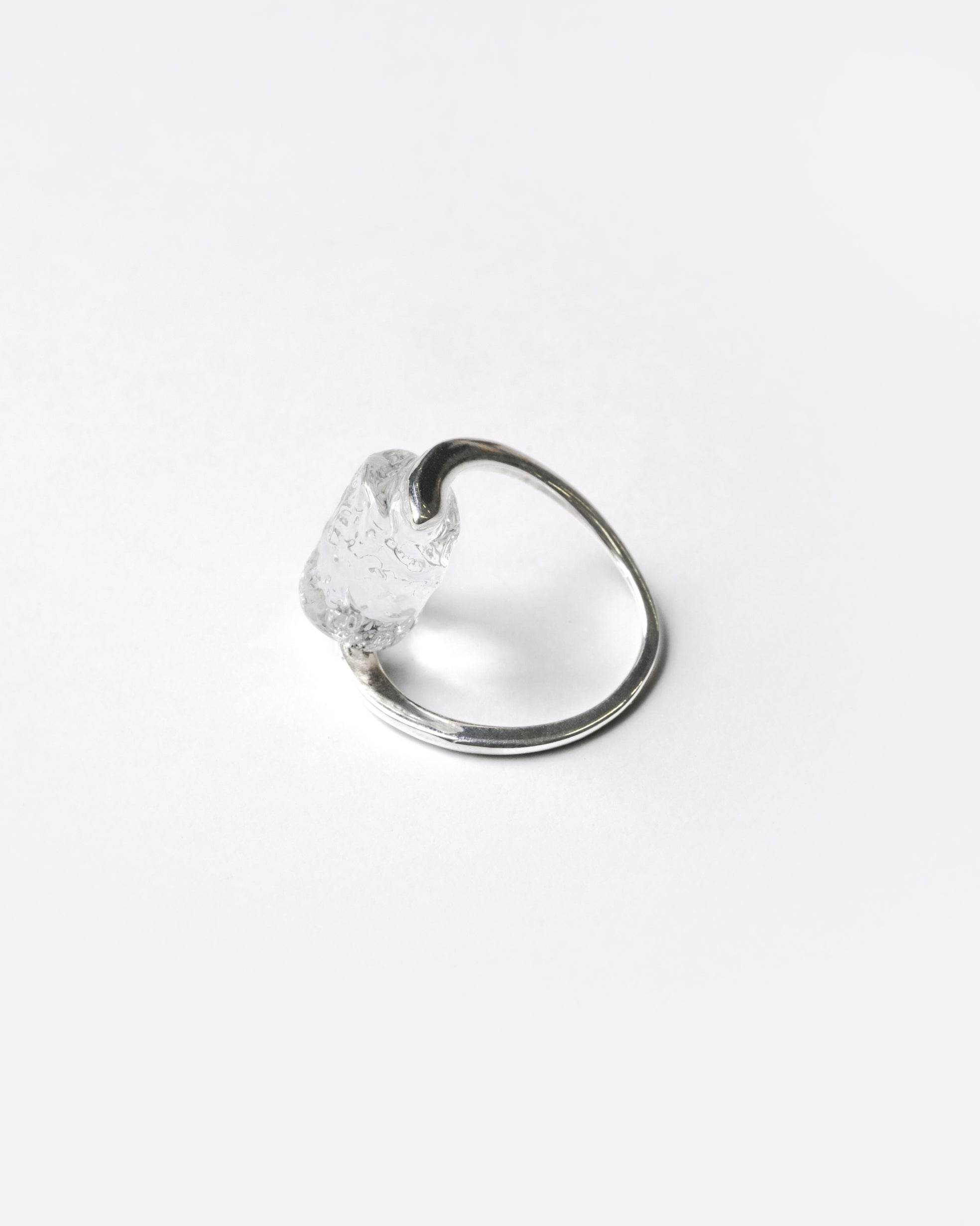 A rhodium‑color plated ring featuring clear glass fragments inspired by melting glaciers, held between two metal bands.
