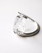 A rhodium‑color plated ring featuring clear glass fragments inspired by melting glaciers, held between two metal bands.