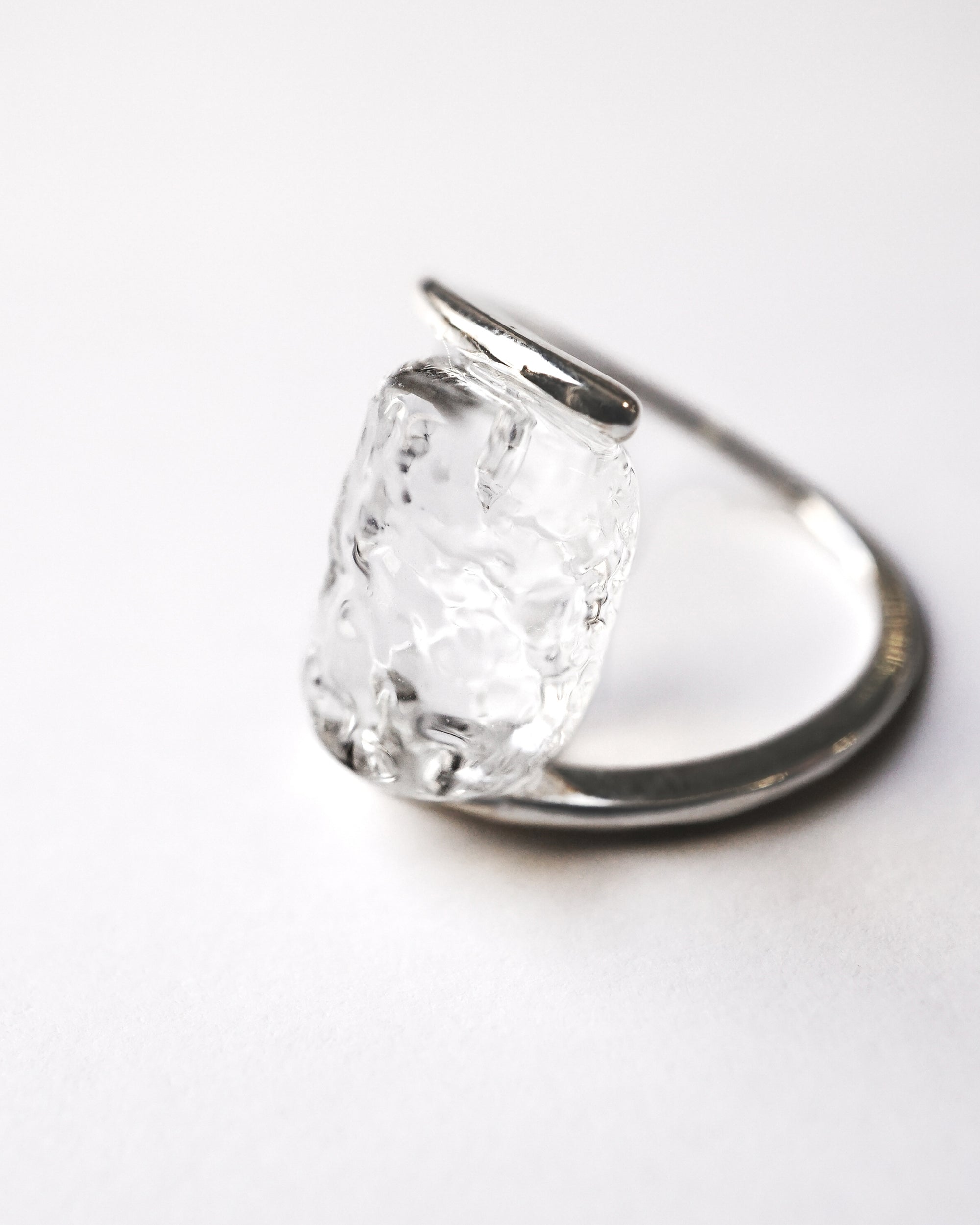 A rhodium‑color plated ring featuring clear glass fragments inspired by melting glaciers, held between two metal bands.