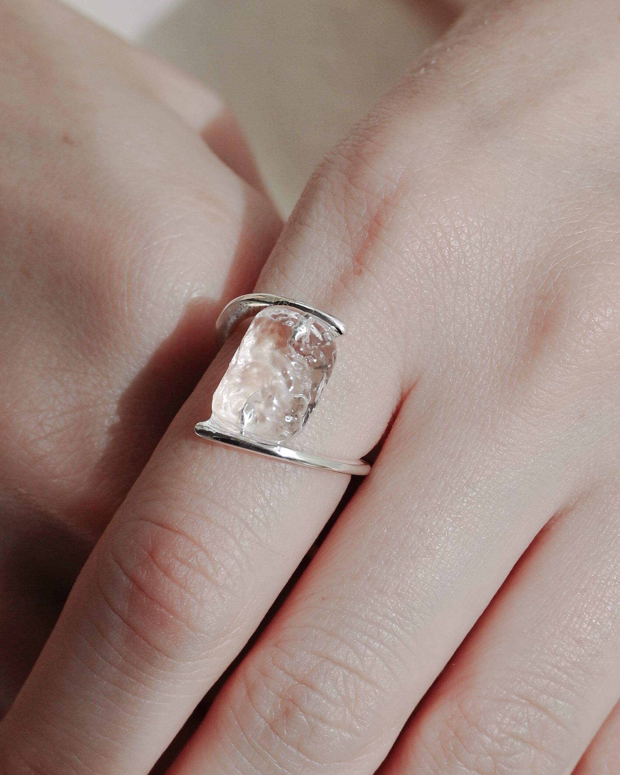 Clear, glacier‑like glass pieces secured between two rhodium‑plated bands in a ring design that curves softly around the finger.