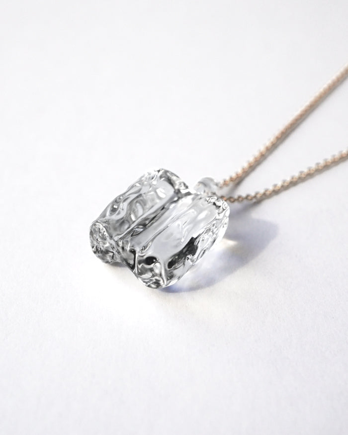 “Clear, glacier‑like glass pieces that catch the light, suspended from an adjustable gold‑plated chain.