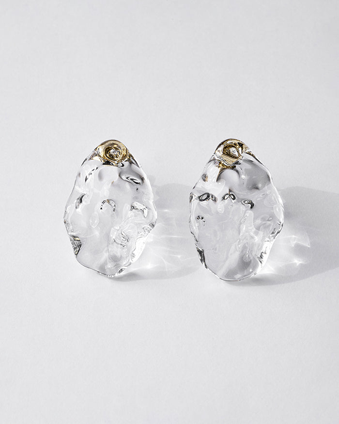 Gold‑plated stud earrings with clear glass shaped like gentle waves of light, shimmering softly like reflections on a lake.