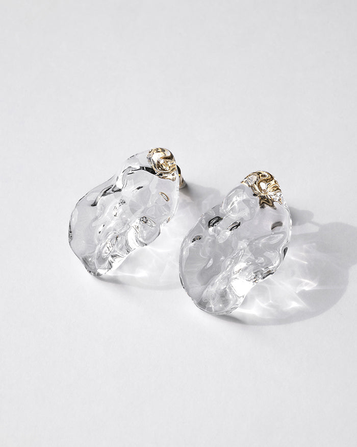 Gold‑plated stud earrings with clear glass shaped like gentle waves of light, shimmering softly like reflections on a lake.