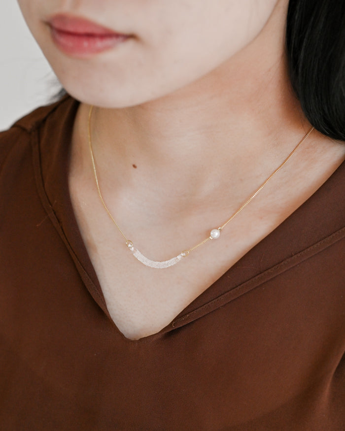 A gold-plated necklace featuring a gentle arch and a textured glass motif, accented with a single freshwater pearl.