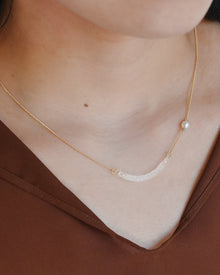 A gold-plated necklace featuring a gentle arch and a textured glass motif, accented with a single freshwater pearl.