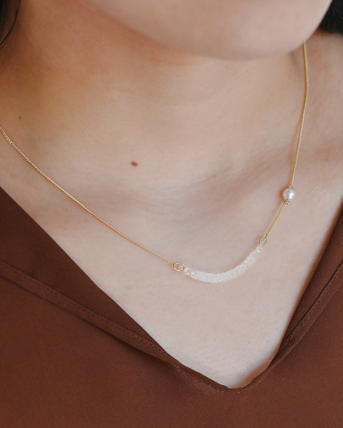 A gold-plated necklace featuring a gentle arch and a textured glass motif, accented with a single freshwater pearl.