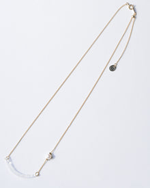A gold‑plated necklace with a gentle arch and a textured glass motif, accented with a single freshwater pearl and featuring an adjustable chain length.