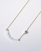 A gold‑plated necklace with a gentle arch and a textured glass motif, accented with a single freshwater pearl and featuring an adjustable chain length.