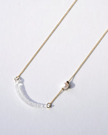 A gold‑plated necklace with a gentle arch and a textured glass motif, accented with a single freshwater pearl and featuring an adjustable chain length.