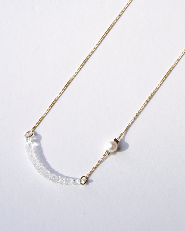 A gold‑plated necklace with a gentle arch and a textured glass motif, accented with a single freshwater pearl and featuring an adjustable chain length.
