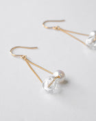 Gold‑plated drop earrings featuring a single freshwater pearl and a small hollow glass sphere suspended from a delicate chain.