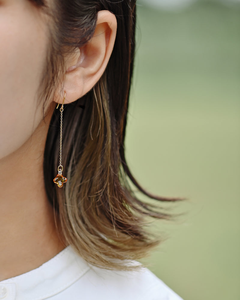A pair of earrings featuring tiny osmanthus-inspired glass blossoms in glossy amber tones. The delicate flowers hang from gold‑plated hooks by fine chains, gently swaying and evoking the soft shimmer and sweet fragrance of osmanthus.