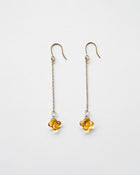 A pair of earrings featuring tiny osmanthus-inspired glass blossoms in glossy amber tones. The delicate flowers hang from gold‑plated hooks by fine chains, gently swaying and evoking the soft shimmer and sweet fragrance of osmanthus.