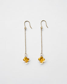 A pair of earrings featuring tiny osmanthus-inspired glass blossoms in glossy amber tones. The delicate flowers hang from gold‑plated hooks by fine chains, gently swaying and evoking the soft shimmer and sweet fragrance of osmanthus.