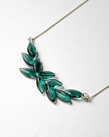 A necklace featuring a gentle arch of fresh green leaves, crafted in glass and suspended from a delicate gold‑plated chain. The design captures the vitality of new spring foliage, as if light has been softly lifted from overlapping leaves and transformed into an accessory.