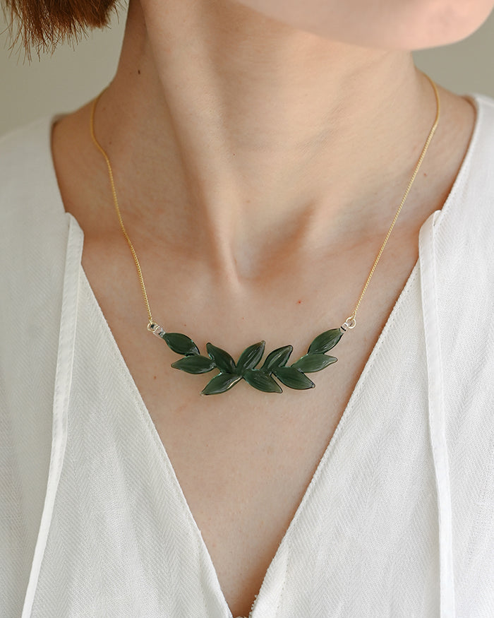A necklace featuring a gentle arch of fresh green leaves, crafted in glass and suspended from a delicate gold‑plated chain. The design captures the vitality of new spring foliage, as if light has been softly lifted from overlapping leaves and transformed into an accessory.