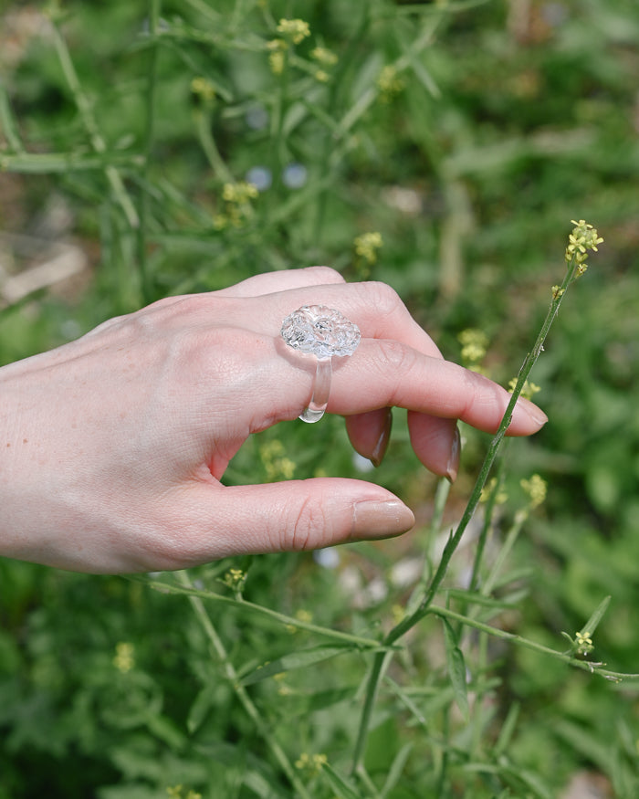 A delicate glass artwork inspired by flowers opening toward the sun, featuring finely shaped translucent petals that reflect light with soft brilliance. A handmade glass ring, carefully shaped by artisans, showcasing clear and luminous glasswork.