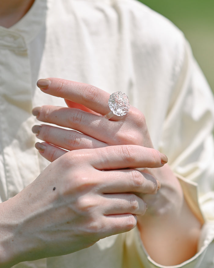 A delicate glass artwork inspired by flowers opening toward the sun, featuring finely shaped translucent petals that reflect light with soft brilliance. A handmade glass ring, carefully shaped by artisans, showcasing clear and luminous glasswork.