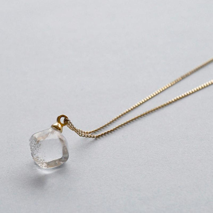 “A soft cube-shaped handmade glass pendant combining textured frosted sides and smooth surfaces, attached to a slender gold chain.