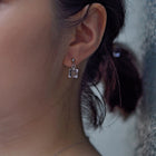Delicate stud earrings with moonlight‑like soft glass cubes, finished in rhodium‑color plating.