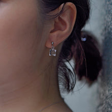 Delicate stud earrings with moonlight‑like soft glass cubes, finished in rhodium‑color plating.