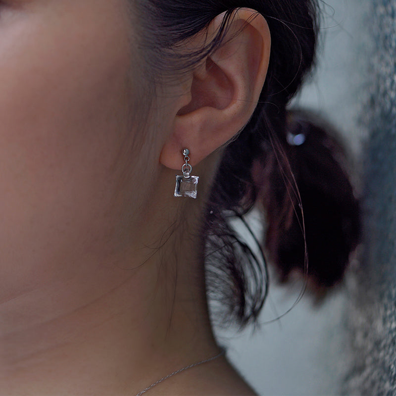 Delicate stud earrings with moonlight‑like soft glass cubes, finished in rhodium‑color plating.
