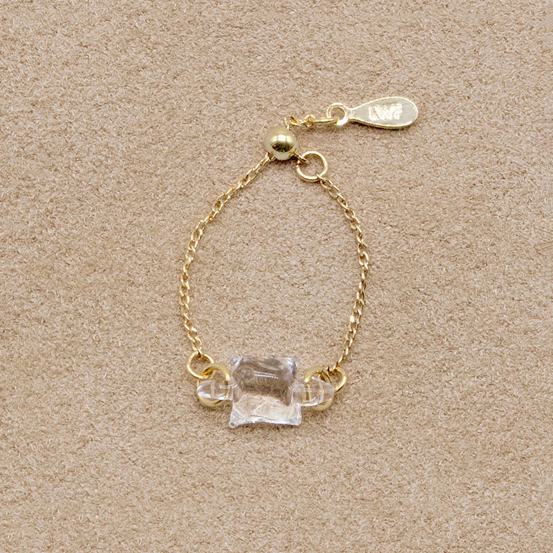 “A gold-plated adjustable ring featuring a soft cube-shaped glass element with contrasting frosted and smooth surfaces that evoke moonlight.