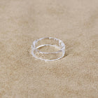 A transparent glass ring featuring gentle wave‑like patterns across its surface, creating a bright, water‑like shine.