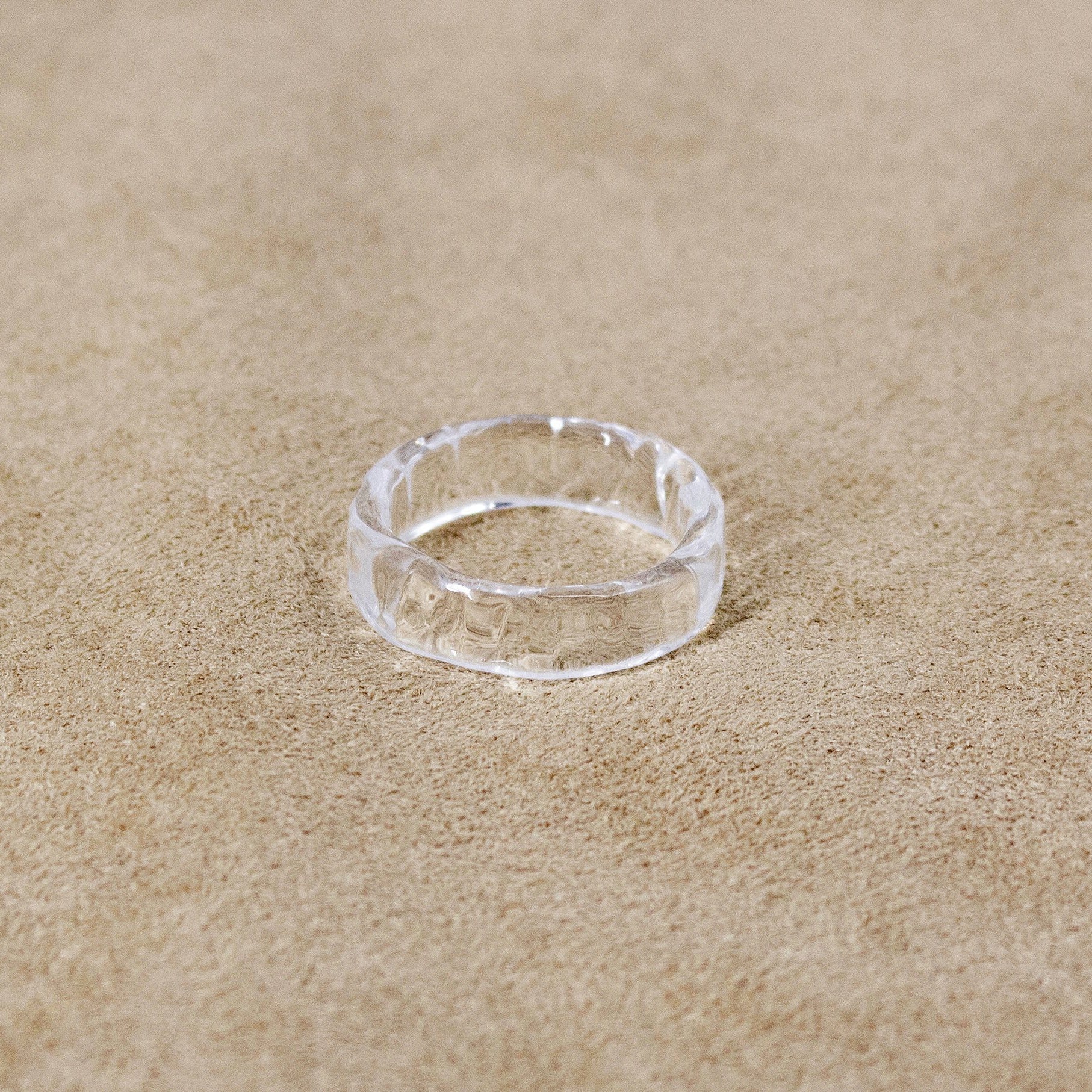 A transparent glass ring featuring gentle wave‑like patterns across its surface, creating a bright, water‑like shine.