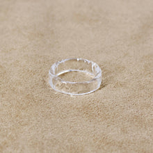 A transparent glass ring featuring gentle wave‑like patterns across its surface, creating a bright, water‑like shine.