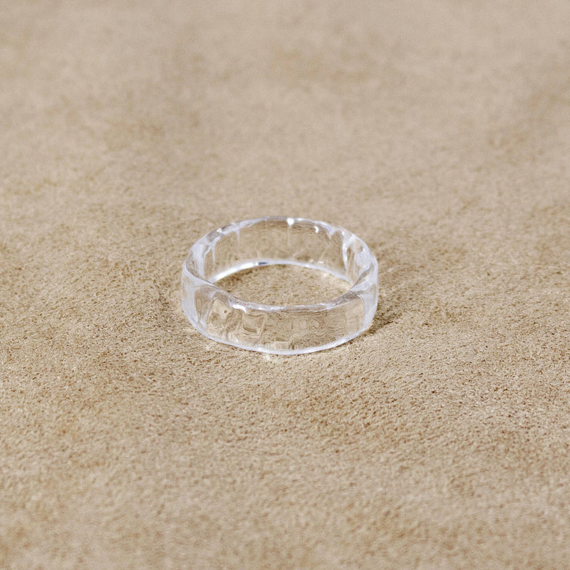 A transparent glass ring featuring gentle wave‑like patterns across its surface, creating a bright, water‑like shine.