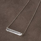 A handmade glass pendant with a lightly textured, frosted finish, hanging from a slender necklace chain.