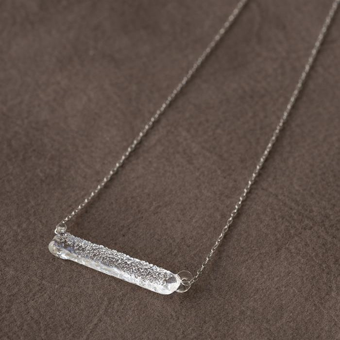 A handmade glass pendant with a lightly textured, frosted finish, hanging from a slender necklace chain.