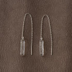 A pair of handmade glass earrings featuring a lightly textured, frosty finish and a long chain that threads through the piercing