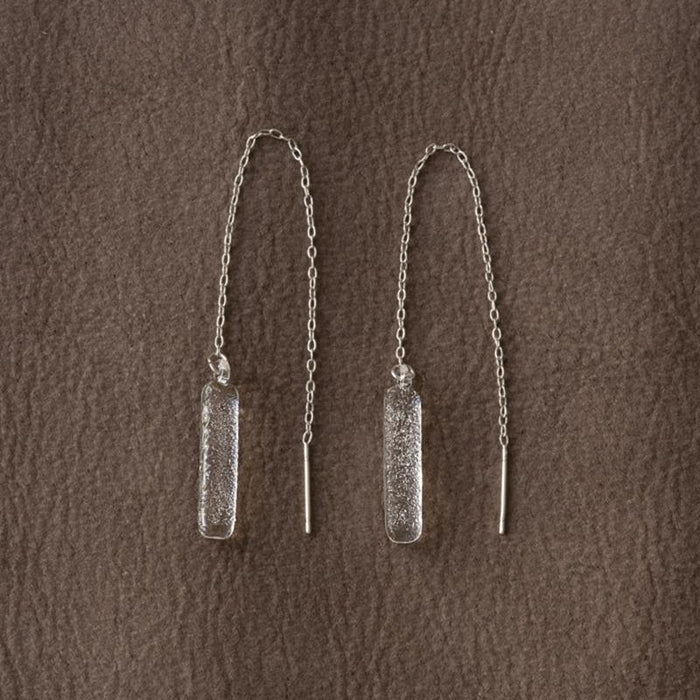 A pair of handmade glass earrings featuring a lightly textured, frosty finish and a long chain that threads through the piercing