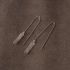 A pair of handmade glass earrings featuring a lightly textured, frosty finish and a long chain that threads through the piercing
