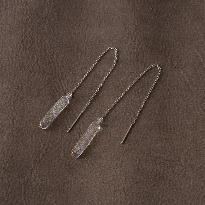 A pair of handmade glass earrings featuring a lightly textured, frosty finish and a long chain that threads through the piercing