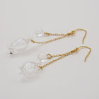 Handmade glass lily earrings with one flower and one bud, both hanging and moving gently from gold‑plated hooks.