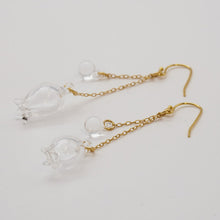 Handmade glass lily earrings with one flower and one bud, both hanging and moving gently from gold‑plated hooks.