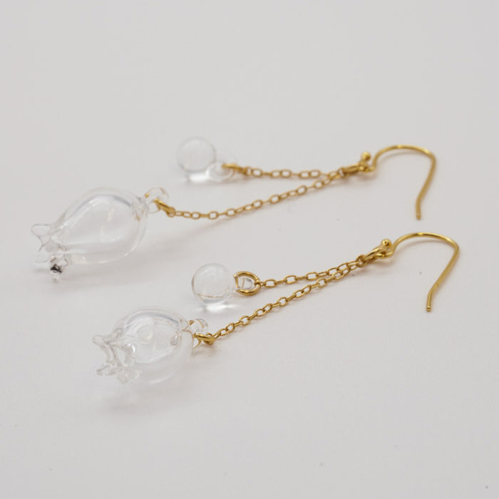Handmade glass lily earrings with one flower and one bud, both hanging and moving gently from gold‑plated hooks.