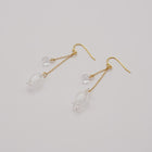 Handmade glass lily earrings with one flower and one bud, both hanging and moving gently from gold‑plated hooks.