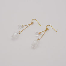 Handmade glass lily earrings with one flower and one bud, both hanging and moving gently from gold‑plated hooks.