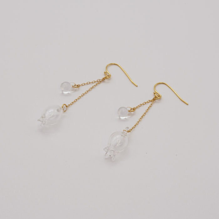 Handmade glass lily earrings with one flower and one bud, both hanging and moving gently from gold‑plated hooks.