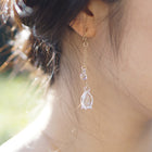 Handmade glass lily earrings with one flower and one bud, both hanging and moving gently from gold‑plated hooks.