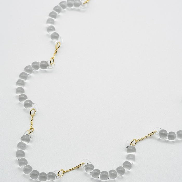 A necklace made of five connected arcs that resemble softly rounded water droplets, attached to a gold‑plated chain with an adjustable sliding ball.