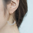 Handmade glass arc pieces resembling gathered water droplets, suspended at both ends by twin gold‑plated chains from a hook.